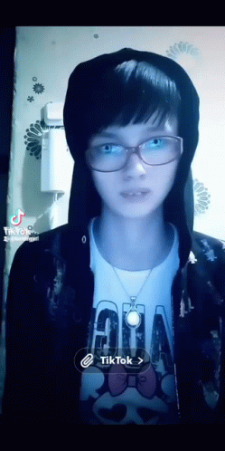 a girl wearing glasses and a hoodie has a tiktok icon on the bottom right