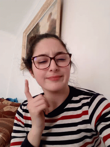 A Girl Wearing Glasses And A Striped Shirt Is Giving A Thumbs Up Sign GIF