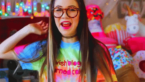 A Girl Wearing Glasses And A Tie Dye Shirt With The Words Wishblog Written On It GIF
