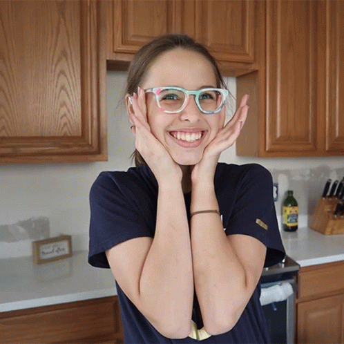 A Girl Wearing Glasses Holds Her Hands To Her Face GIF