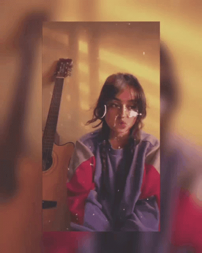 A Girl With A Bandage On Her Face Stands Next To An Acoustic Guitar GIF