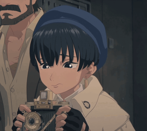 A Girl With A Blue Hat Is Holding A Small Camera GIF