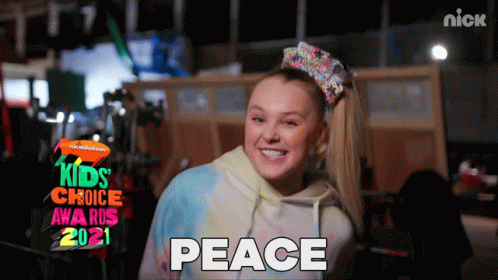 A Girl With A Bow In Her Hair Is Smiling In Front Of A Sign That Says Kids Choice Awards 2021 GIF