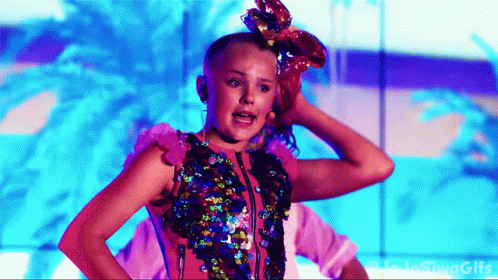 A Girl With A Bow In Her Hair Is Standing In Front Of A Blue Wall . GIF
