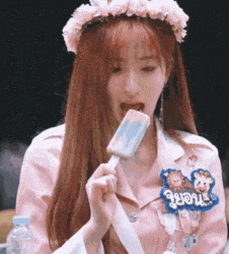 A Girl With A Flower Crown On Her Head Is Eating An Ice Cream Bar . GIF