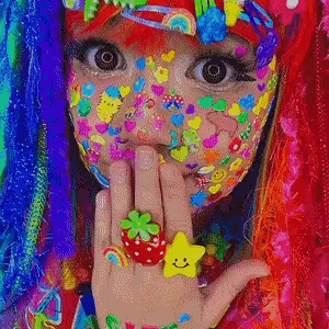 A Girl With A Lot Of Colorful Stickers On Her Face Is Wearing A Strawberry Ring And A Star Ring . GIF