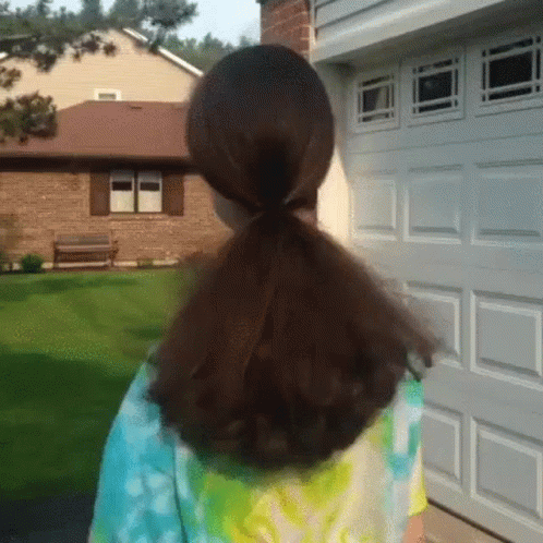 A Girl With A Ponytail Is Standing In Front Of A Garage Door . GIF