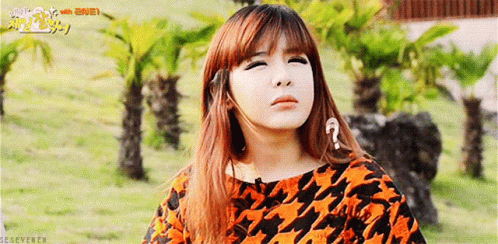 A Girl With A Question Mark On Her Forehead Is Standing In A Field With Palm Trees . GIF