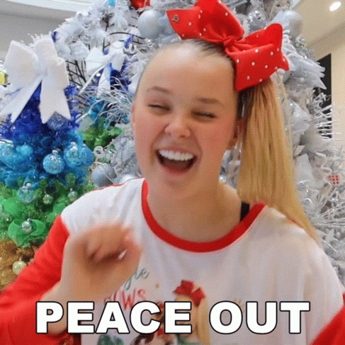 A Girl With A Red Bow In Her Hair Is Laughing In Front Of A Christmas Tree With The Words Peace Out Below Her GIF