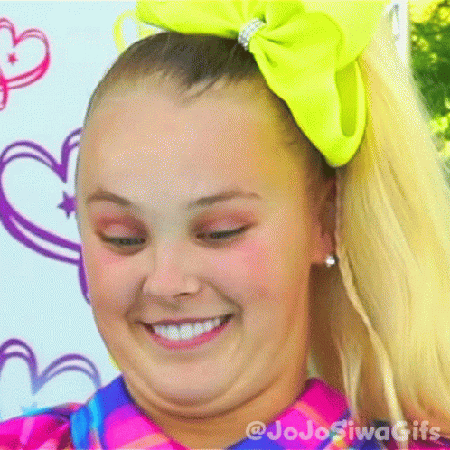 A Girl With A Yellow Bow In Her Hair Is Smiling And Making A Face . GIF