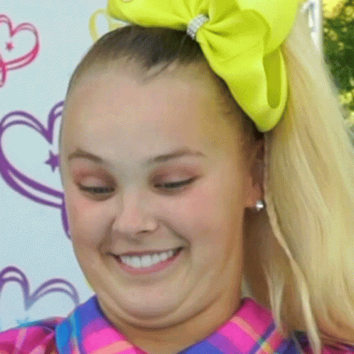 A Girl With A Yellow Bow In Her Hair Smiles For The Camera GIF
