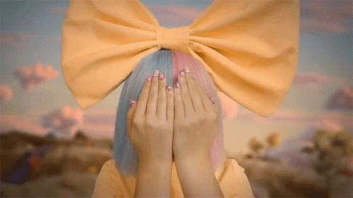 A Girl With A Yellow Bow On Her Head Covers Her Face With Her Hands GIF
