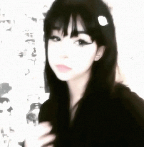 A Girl With Black Hair And Bangs Is Wearing A Black Hoodie And A Flower In Her Hair . GIF