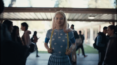 A Girl With Blonde Hair And A Blue Shirt Is Standing In A Hallway GIF