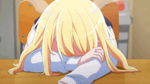A Girl With Blonde Hair Is Laying On A Desk With Her Head On Her Arm GIF