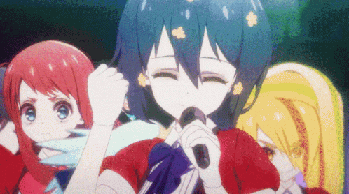 A Girl With Blue Hair Is Singing Into A Microphone In Front Of Two Other Girls GIF