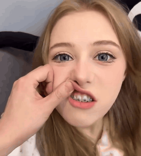 A Girl With Braces On Her Teeth Is Being Touched By A Person GIF