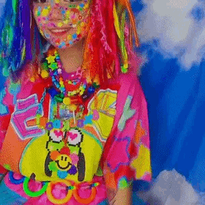 A Girl With Colorful Hair And Face Paint Is Wearing A Colorful Shirt And Necklaces . GIF