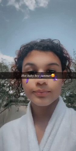 A Girl With Curly Hair Is Wearing A White Robe And A Snapchat Filter That Says Hot Baby Boy Summer GIF