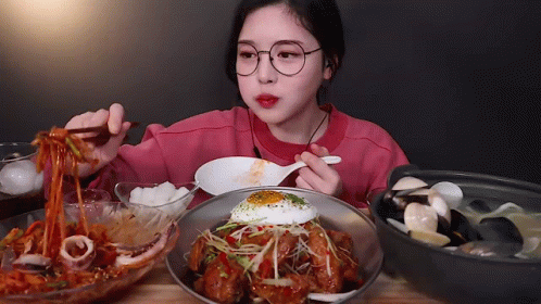 A Girl With Glasses Is Eating Noodles With Chopsticks GIF