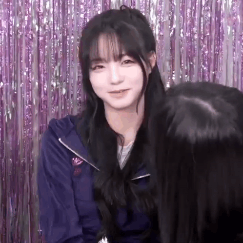 A Girl With Long Black Hair And Bangs Is Standing In Front Of A Purple Curtain . GIF