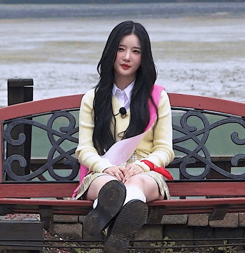 A Girl With Long Black Hair Is Sitting On A Bench With Her Legs Crossed GIF