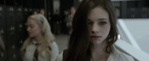 A Girl With Long Dark Hair Looks At The Camera In A Dark Room GIF