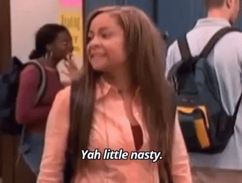 A Girl With Long Hair And A Backpack Is Standing In A Hallway And Says `` Yah Little Nasty '' . GIF