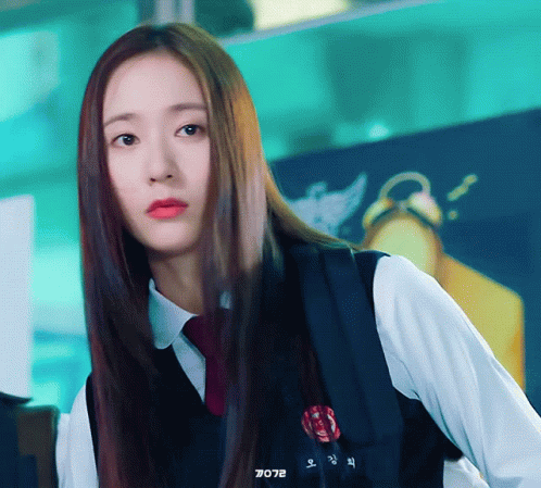 A Girl With Long Hair Is Wearing A White Shirt And A Black Vest With A Red Badge On It GIF