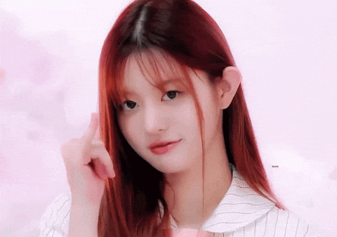 A Girl With Long Red Hair Is Looking At The Camera And Pointing At Her Hair GIF