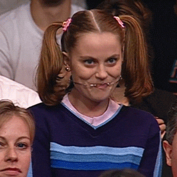 A Girl With Pigtails And Braces On Her Teeth Is Making A Funny Face While Sitting In A Crowd . GIF