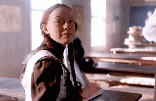A Girl With Pigtails Is Sitting At A Desk With A Book GIF