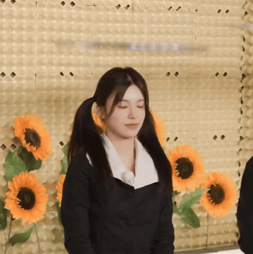 A Girl With Pigtails Stands In Front Of A Wall With Sunflowers GIF