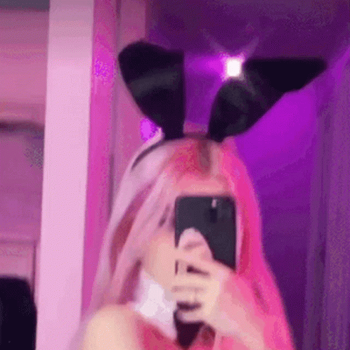 A Girl With Pink Hair Is Taking A Selfie With Her Phone While Wearing Bunny Ears . GIF