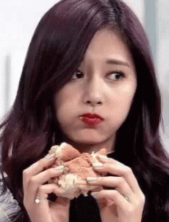 A Girl With Purple Hair Is Eating A Hamburger With Her Mouth Open . GIF