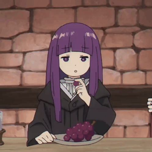a girl with purple hair sits at a table with a plate of grapes on it