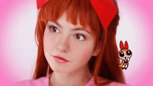 A Girl With Red Hair And A Red Bow On Her Head Is Wearing A Pink Shirt . GIF