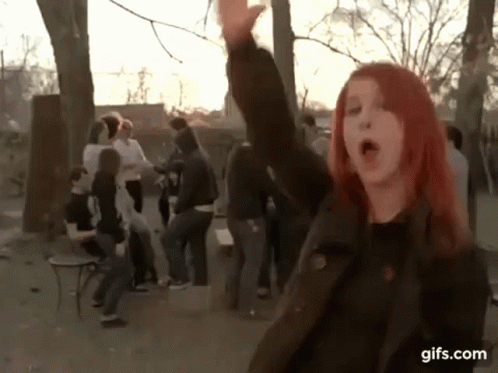 A Girl With Red Hair Is Standing In Front Of A Group Of People With Her Hand In The Air .. GIF