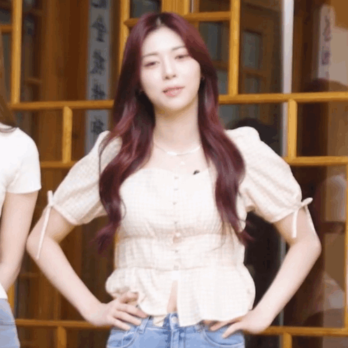 A Girl With Red Hair Is Standing With Her Hands On Her Hips In Front Of A Window GIF