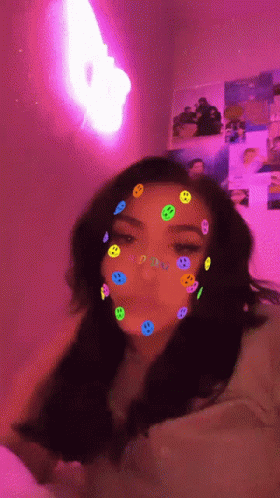 A Girl With Smiley Faces On Her Face And A Pink Light In The Background GIF