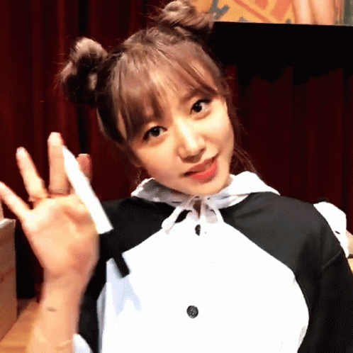 A Girl With Two Buns On Her Hair Is Waving Her Hand GIF