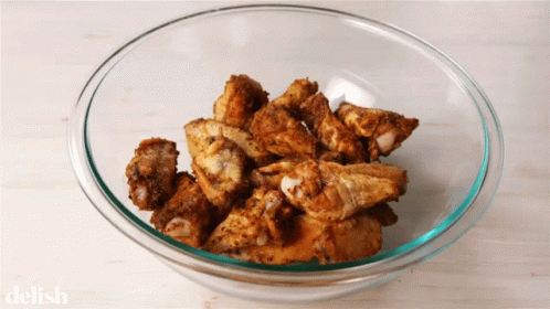 A Glass Bowl Filled With Fried Chicken Wings With The Word Delish On The Bottom GIF