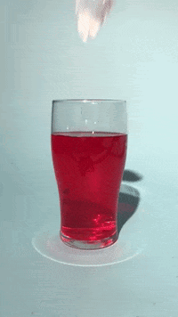 A Glass Filled With Red Liquid With A Strawberry Splashing Out Of It GIF