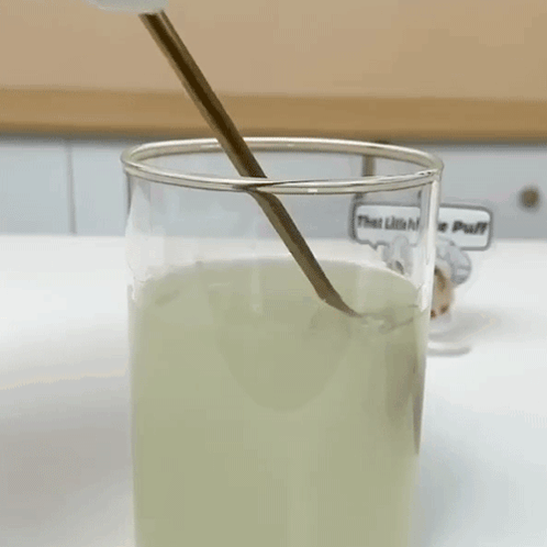 A Glass Of Liquid With A Spoon In It And A Sticker That Says That Little Puff GIF