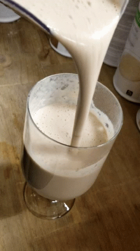A Glass Of Milk Is Being Poured Into A Glass On A Wooden Table GIF