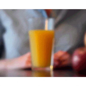 A Glass Of Orange Juice Is On A Table Next To Apples GIF