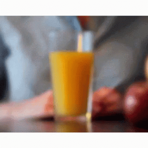 A Glass Of Orange Juice Is Sitting On A Table GIF
