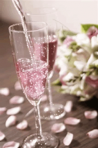 A Glass Of Pink Champagne Is Being Poured Into A Glass On A Table . GIF