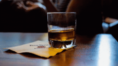 A Glass Of Whiskey Sits On A Napkin With Four Roses Written On It GIF