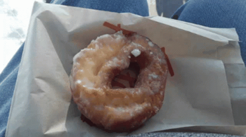 A Glazed Donut Is Sitting On A Piece Of Paper GIF
